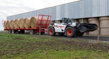 Телескопический погрузчик для сельского хозяйства Bobcat TL43.80HF+AGRI перемещает прицеп со снопами по ферме.